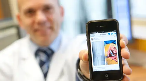 Foto del Dr. Mora con el móvil Foto difuminada del Dr. Gonzalo Mora con el móvil en la mano enseñándolo a cámara