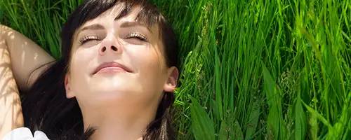 Consejos mente y salud. Felicidad. Clínica Universidad de Navarra Imagen de una mujer relajada y sonriente tumbada en el campo.