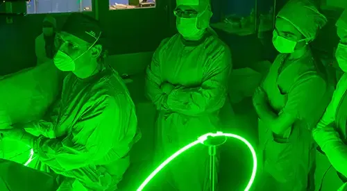 Un cirujano trata la hiperplasia benigna de próstata mediante láser verde, mientras varios especialistas observan el procedimiento.
