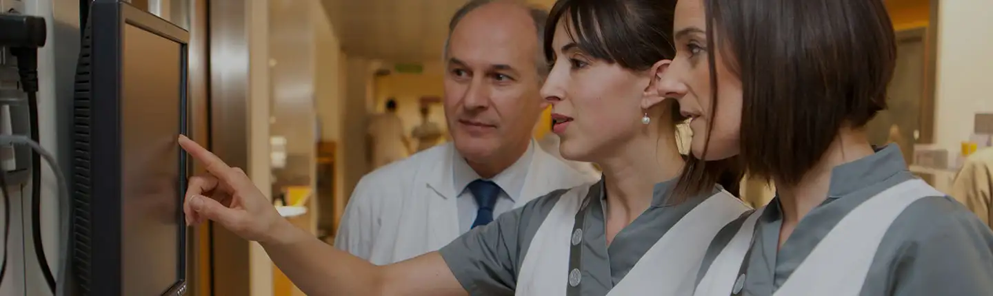 Una enfermera señala un monitor mientras otra enfermera y un médico observan a su lado.