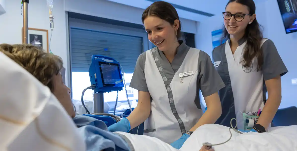 Imagen de una enfermera especializada, junto a una estudiante de Enfermería, atendiendo a una paciente hospitalizada en la planta de Oncología de la Clínica Universidad de Navarra.